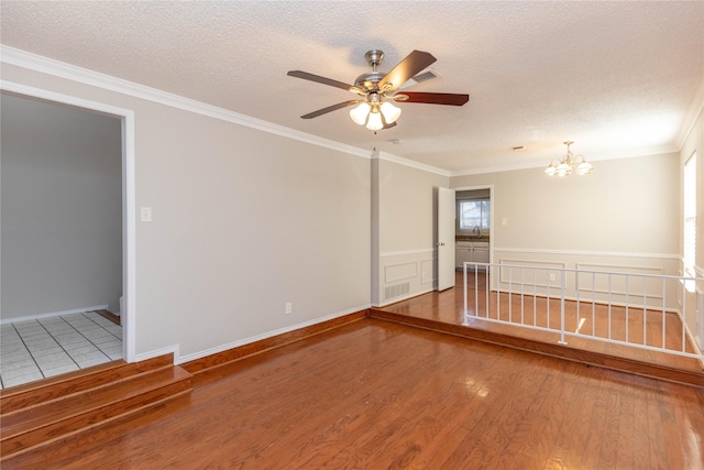 spare room with ceiling fan with notable chandelier, a textured ceiling, wood finished floors, wainscoting, and crown molding