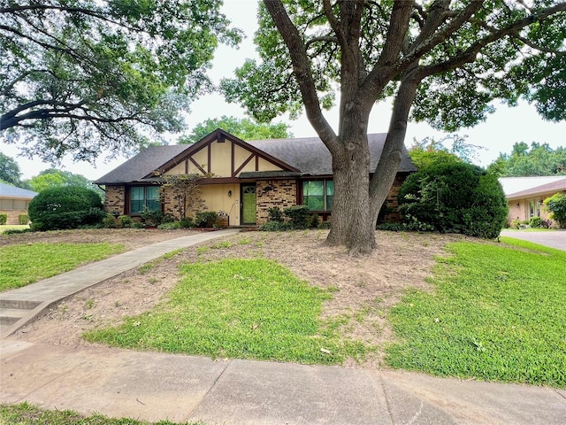 tudor-style house with a shingled roof, a front yard, brick siding, and stucco siding