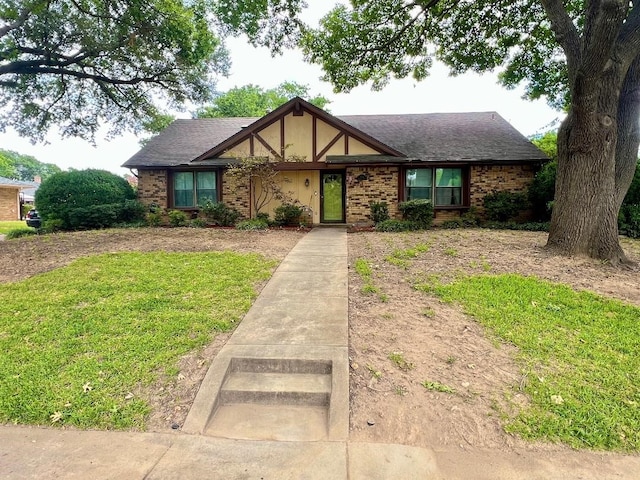 tudor home featuring a shingled roof, brick siding, a front lawn, and stucco siding