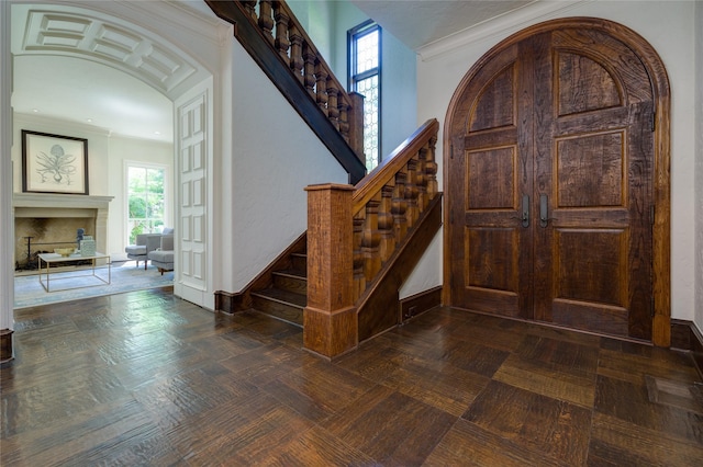 entrance foyer featuring ornamental molding, arched walkways, and a fireplace with raised hearth