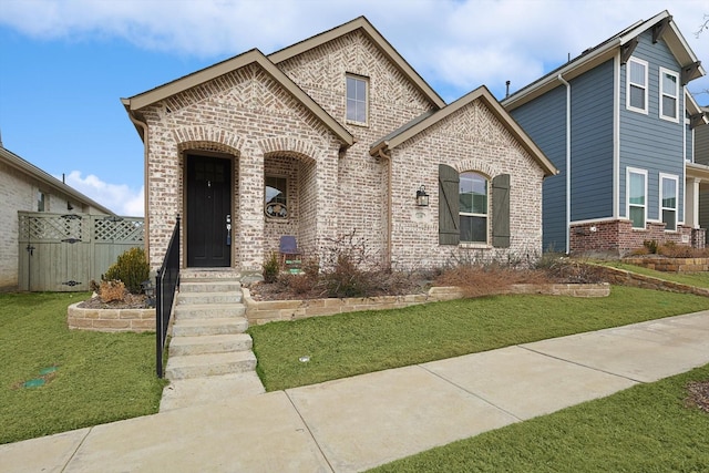 view of front of house with brick siding, a front lawn, and fence