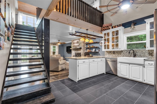 kitchen with a ceiling fan, a sink, stainless steel dishwasher, a peninsula, and glass insert cabinets