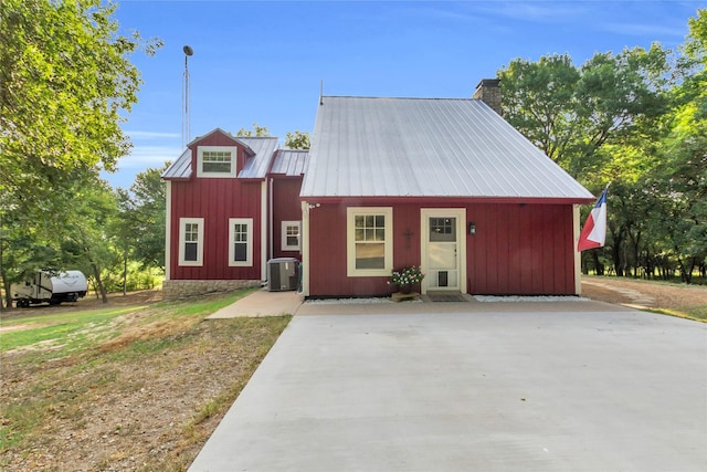 view of front of home with central air condition unit, metal roof, driveway, and a chimney