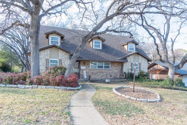 view of front of home featuring stone siding, a front lawn, and roof with shingles