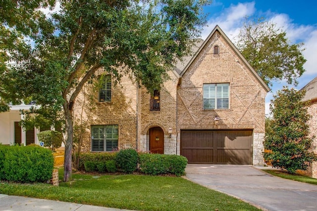 tudor-style house featuring brick siding, a front yard, a garage, stone siding, and driveway