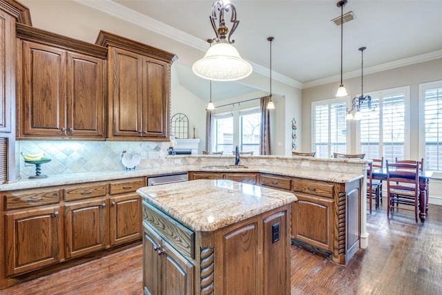 kitchen featuring brown cabinetry, a center island, pendant lighting, and visible vents