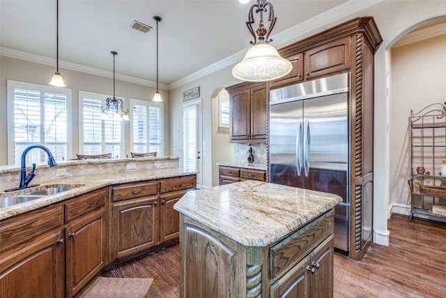 kitchen with arched walkways, ornamental molding, a center island, stainless steel built in fridge, and a sink