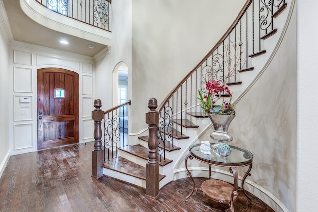 entryway featuring a towering ceiling, arched walkways, wood finished floors, and ornamental molding