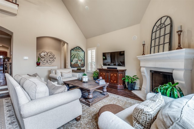 living room featuring a fireplace with raised hearth, high vaulted ceiling, arched walkways, and wood finished floors