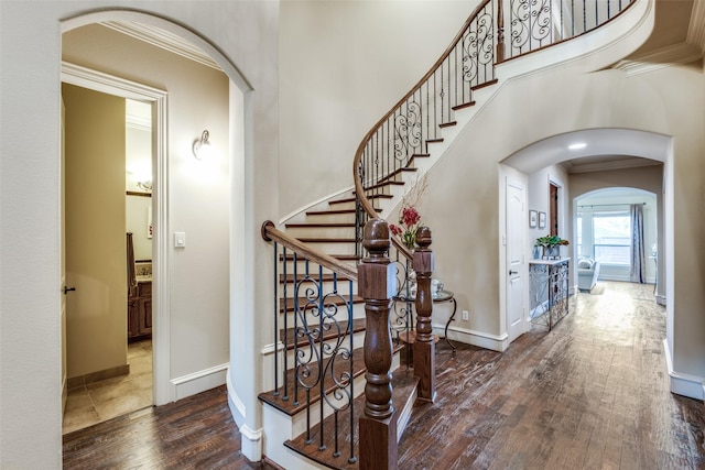 interior space with arched walkways, a towering ceiling, baseboards, ornamental molding, and dark wood finished floors