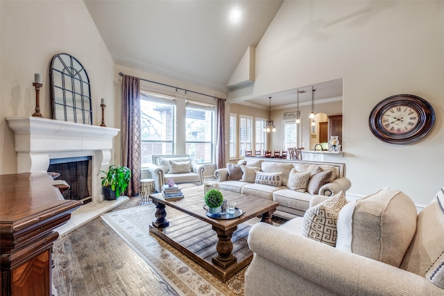 living area featuring a fireplace with raised hearth, high vaulted ceiling, ornamental molding, and light wood-type flooring