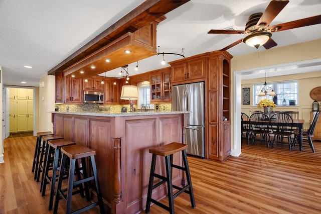 kitchen with light wood-style floors, appliances with stainless steel finishes, light stone countertops, a kitchen bar, and glass insert cabinets