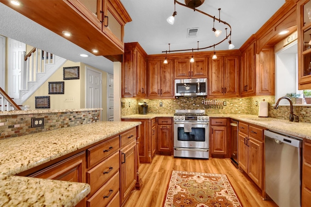 kitchen featuring stainless steel appliances, light stone counters, a sink, and glass insert cabinets