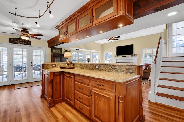 kitchen featuring visible vents, a ceiling fan, brown cabinets, open floor plan, and light stone countertops