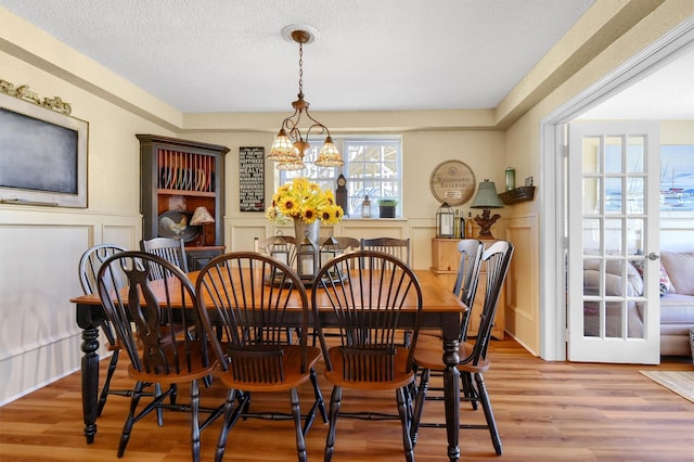 dining area featuring a textured ceiling, a wainscoted wall, light wood-type flooring, and a decorative wall