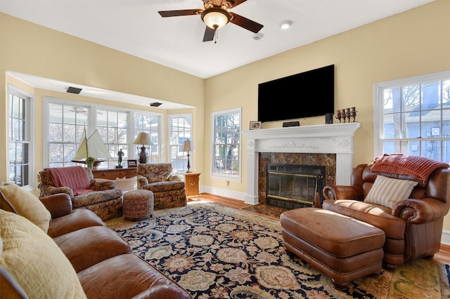 living area featuring a healthy amount of sunlight, a premium fireplace, baseboards, and wood finished floors