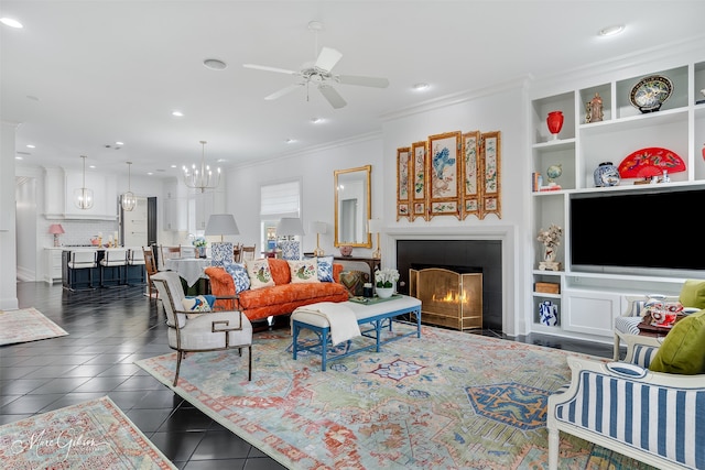 living room featuring built in features, crown molding, a tiled fireplace, dark tile patterned flooring, and ceiling fan with notable chandelier