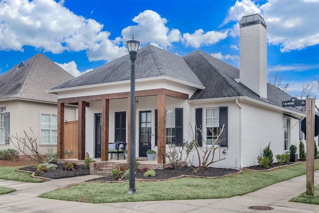 view of front of home with a porch, roof with shingles, a chimney, and brick siding