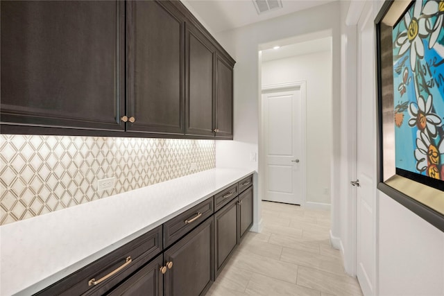 interior space featuring tasteful backsplash, light countertops, visible vents, dark brown cabinets, and baseboards