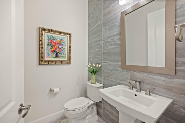 bathroom with tile walls, tasteful backsplash, toilet, a sink, and baseboards