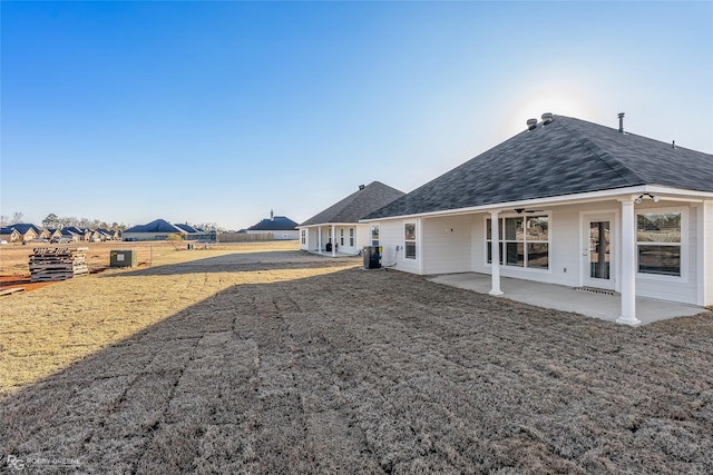 back of property with a lawn, a ceiling fan, a patio, roof with shingles, and fence