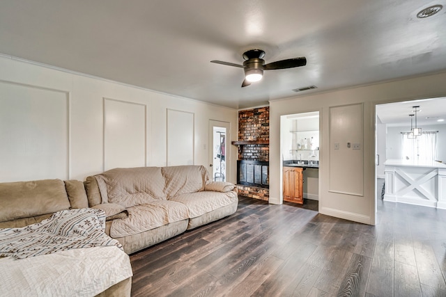 living room featuring a brick fireplace, ornamental molding, a decorative wall, and dark wood-type flooring