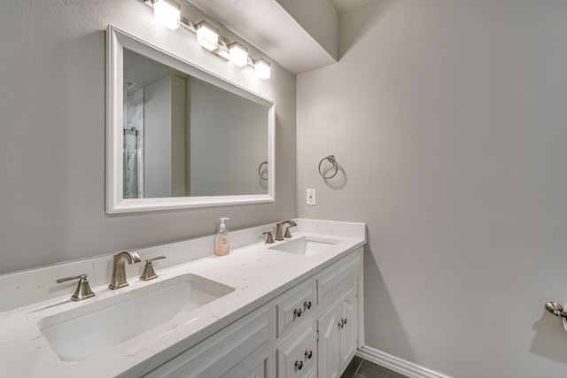 full bath with double vanity, a sink, and baseboards