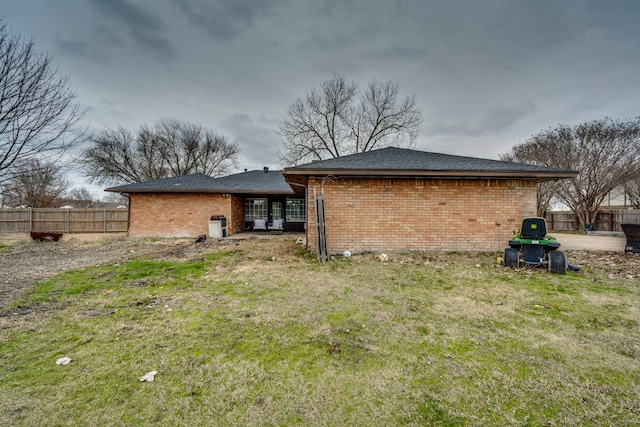 rear view of house featuring a yard, brick siding, and fence