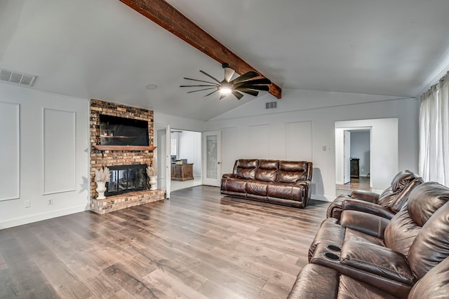 living area featuring vaulted ceiling with beams, a decorative wall, a fireplace, wood finished floors, and visible vents