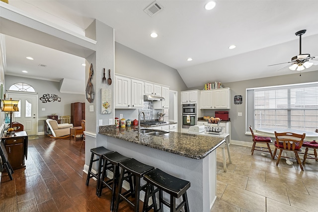 kitchen featuring visible vents, a peninsula, white cabinetry, and under cabinet range hood