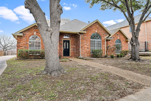 view of front of home with brick siding, a shingled roof, and fence