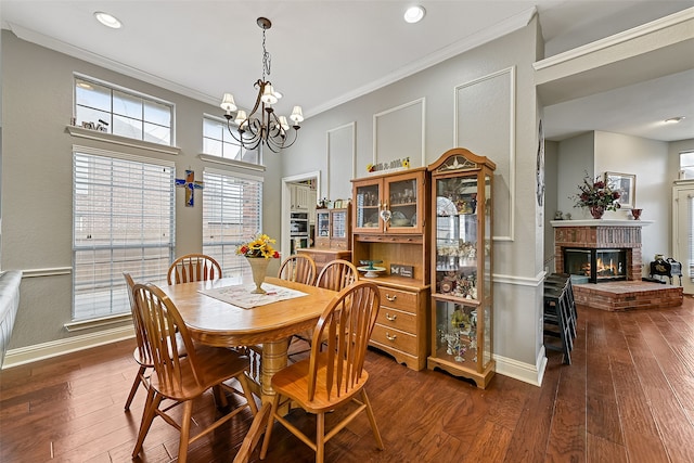 dining area with dark wood-style floors, a brick fireplace, ornamental molding, and a notable chandelier