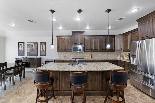 kitchen featuring dark brown cabinetry, a center island with sink, appliances with stainless steel finishes, and pendant lighting