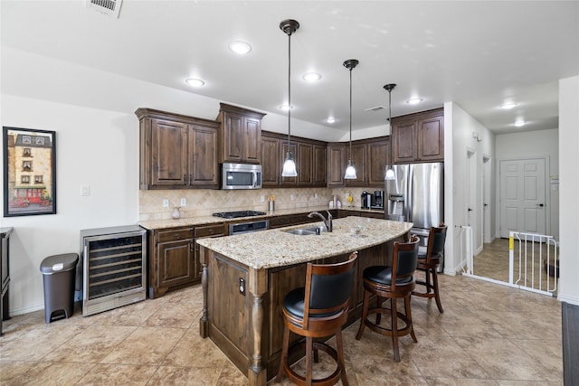 kitchen with wine cooler, decorative light fixtures, stainless steel appliances, a sink, and a center island with sink