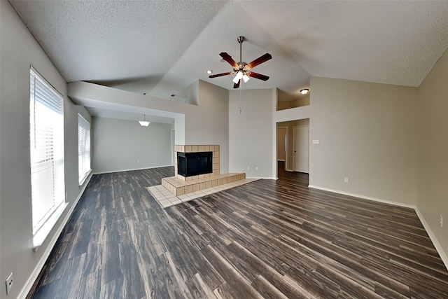 unfurnished living room featuring dark wood-style flooring, vaulted ceiling, a textured ceiling, a tile fireplace, and baseboards