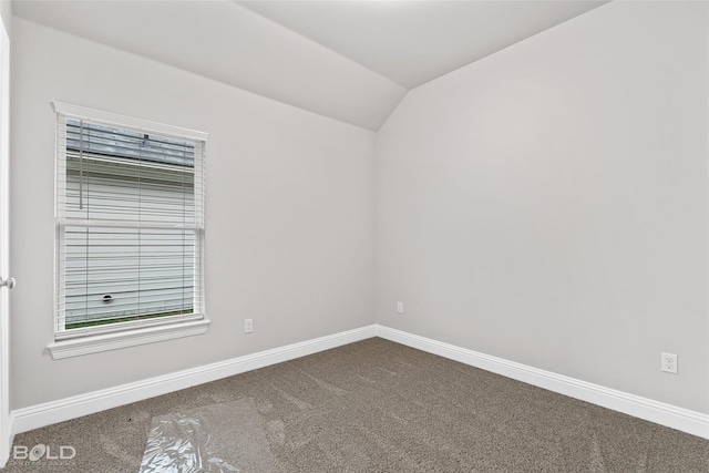 spare room with dark carpet, vaulted ceiling, and baseboards