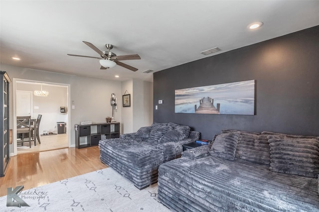 living area with ceiling fan with notable chandelier, visible vents, recessed lighting, and wood finished floors