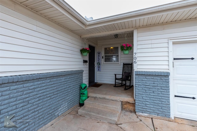 property entrance with covered porch, brick siding, and an attached garage