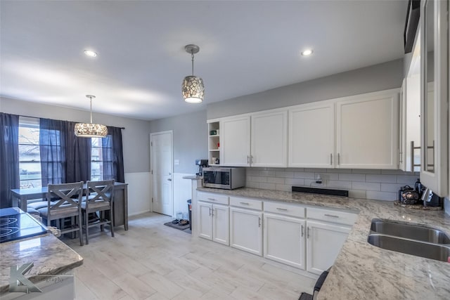 kitchen featuring stainless steel microwave, a sink, white cabinetry, and decorative light fixtures