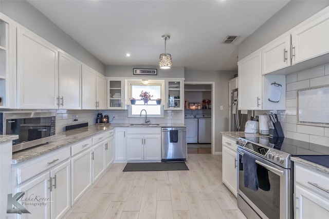 kitchen with visible vents, appliances with stainless steel finishes, independent washer and dryer, white cabinetry, and a sink