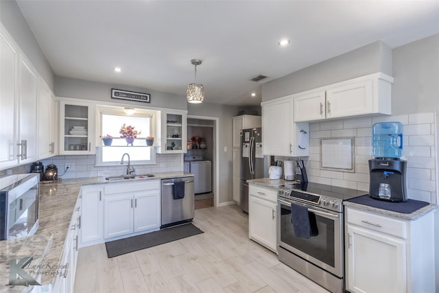 kitchen featuring light stone counters, appliances with stainless steel finishes, white cabinetry, a sink, and washer / dryer