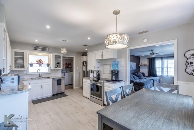 kitchen featuring stainless steel appliances, a sink, white cabinets, light stone countertops, and washer / clothes dryer