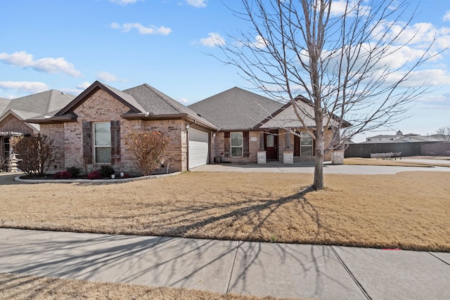 view of front of home with brick siding, a shingled roof, a garage, driveway, and a front lawn