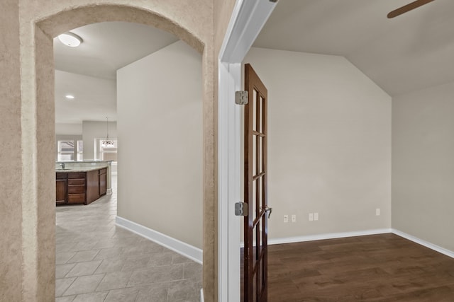 corridor with arched walkways, wood finished floors, lofted ceiling, and baseboards