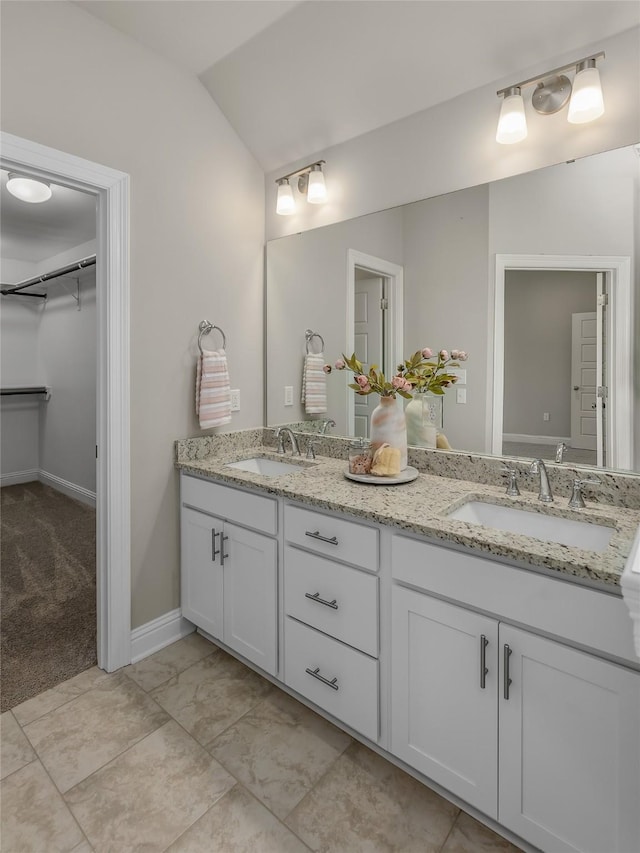 bathroom featuring lofted ceiling, a sink, a spacious closet, and double vanity