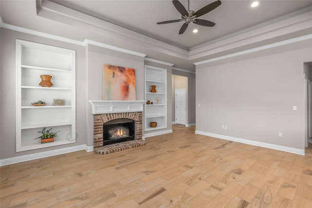 unfurnished living room with light wood finished floors, a fireplace, baseboards, and a tray ceiling