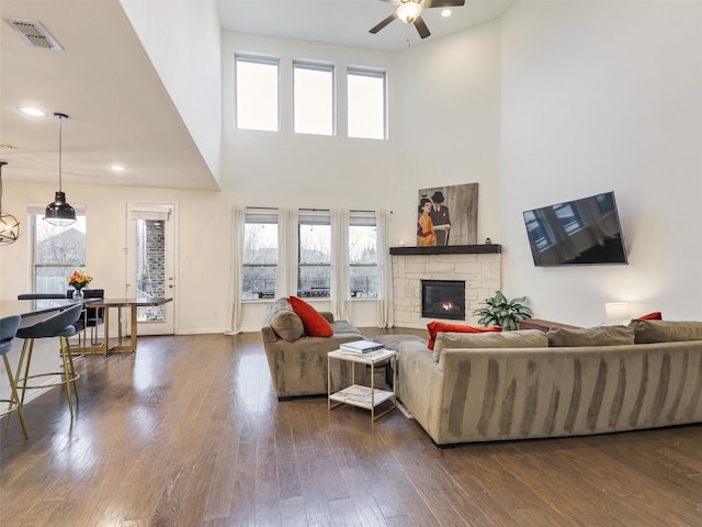 living room featuring a stone fireplace, dark wood-style flooring, plenty of natural light, and visible vents