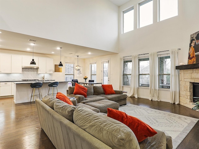 living area featuring visible vents, dark wood-style flooring, a healthy amount of sunlight, and a stone fireplace