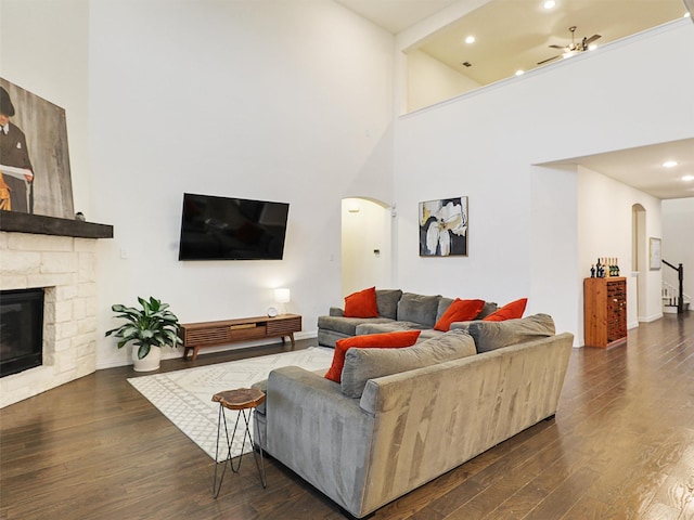 living room with dark wood-style floors, arched walkways, a fireplace, a towering ceiling, and a ceiling fan