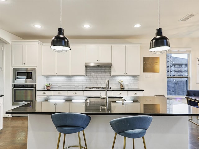 kitchen with appliances with stainless steel finishes, dark countertops, and a center island with sink